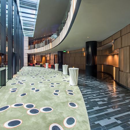 Crowne Plaza Changi Airport By Ihg Singapore Exterior photo The photo shows a modern indoor space that features a curved hallway with a mix of materials and textures. The floor is divided into two sections: one has a smooth, dark tiled design, while the other has a soft, green carpet with circular patterns in