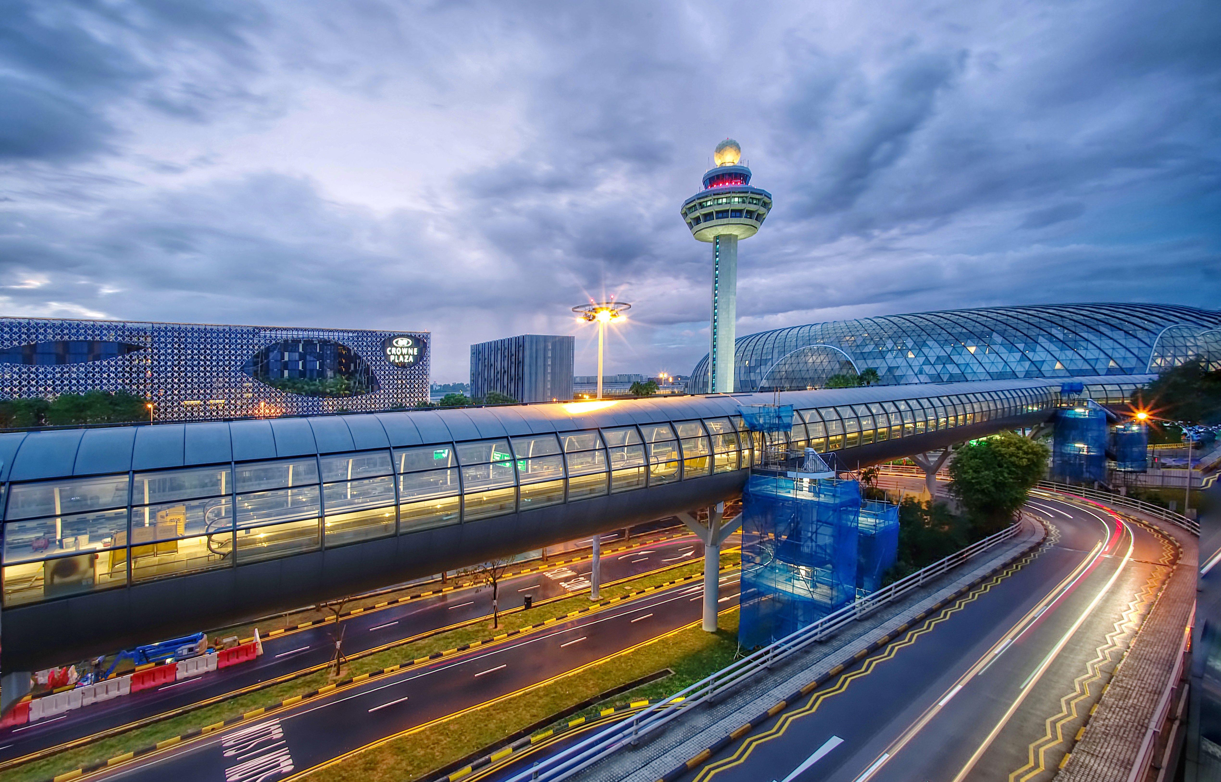 Crowne Plaza Changi Airport By Ihg Singapore Exterior photo The photo depicts an airport scene, likely featuring a modern terminal structure with a distinctive, futuristic design. In the foreground, there is a pedestrian bridge or walkway, along with roads leading to the terminal. A control tower can be seen 