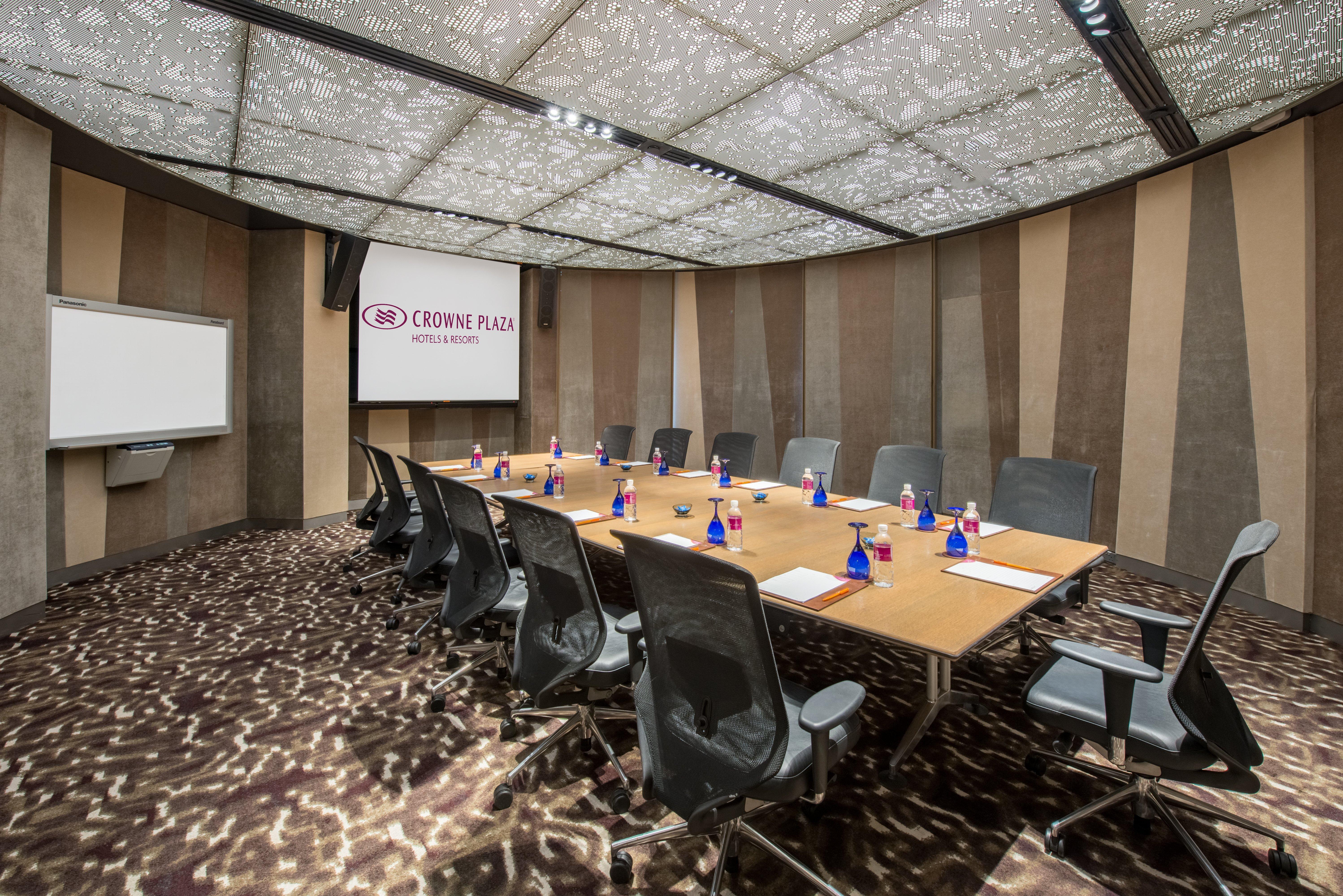 Crowne Plaza Changi Airport By Ihg Singapore Exterior photo The photo shows a modern conference room. It features a large, rectangular wooden table surrounded by ergonomic black office chairs. On the table, there are small blue vases, each containing flowers. The room has a unique, patterned ceiling that enha