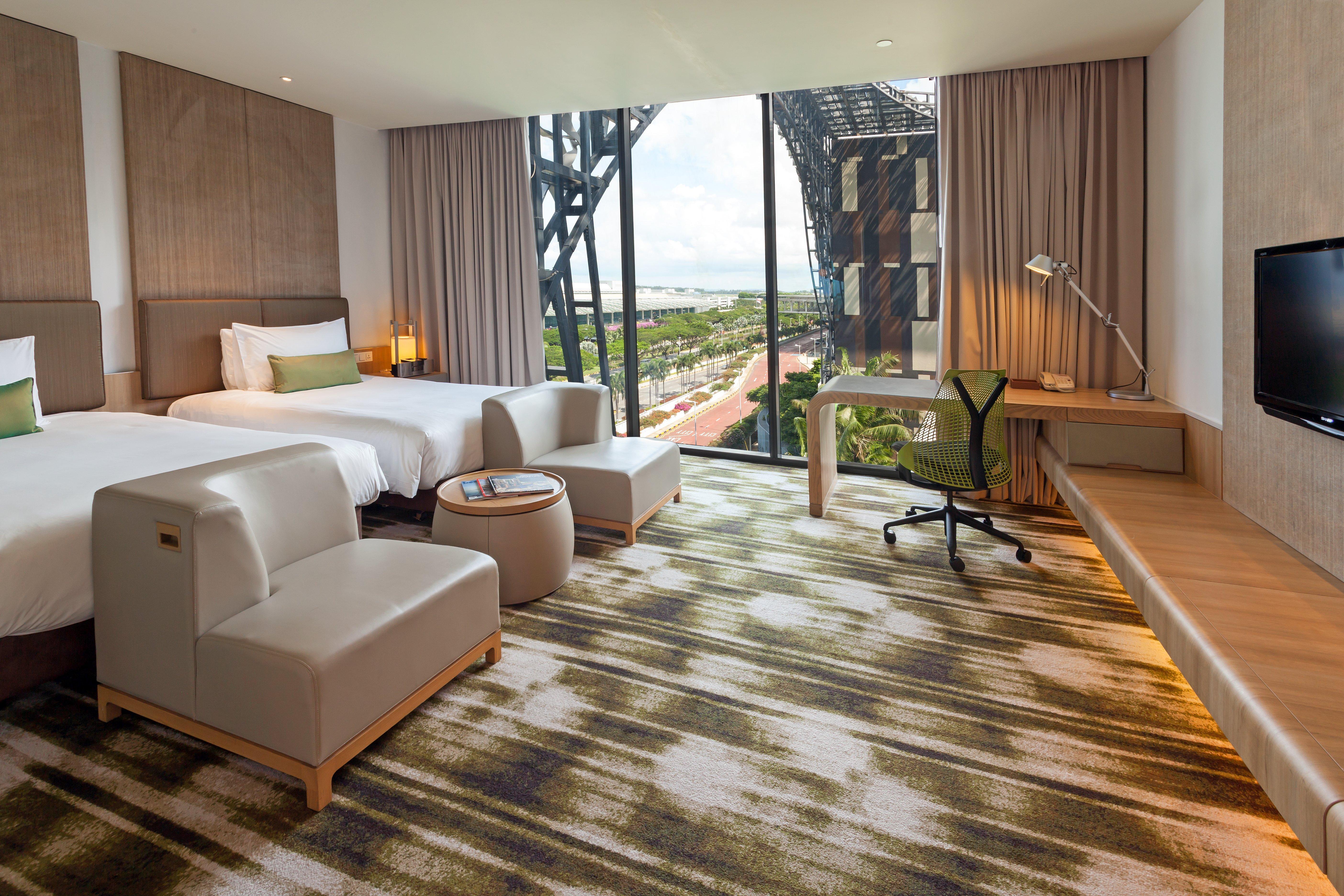 Crowne Plaza Changi Airport By Ihg Singapore Exterior photo The photo depicts a modern hotel room featuring two beds with white linens and a clean, minimalist design. There are two stylish armchairs and a small round table, creating a cozy seating area. The room includes a large window that offers a view of t