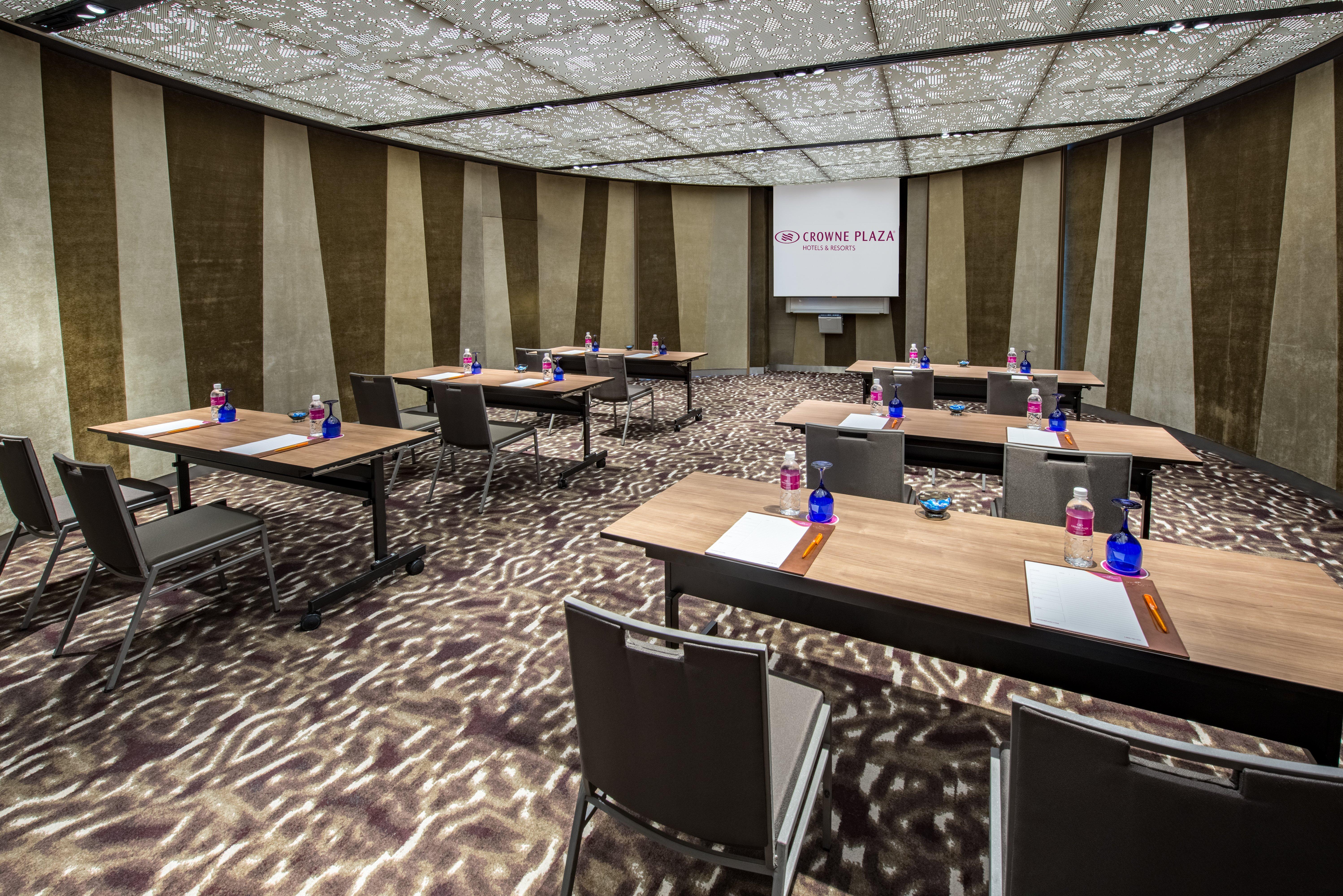 Crowne Plaza Changi Airport By Ihg Singapore Exterior photo The photo shows a modern conference room set up for a meeting or presentation. There are several wooden tables arranged in a U-shape, each equipped with a notepad and pen. Bottled water is placed in blue containers on the tables. The room features a 