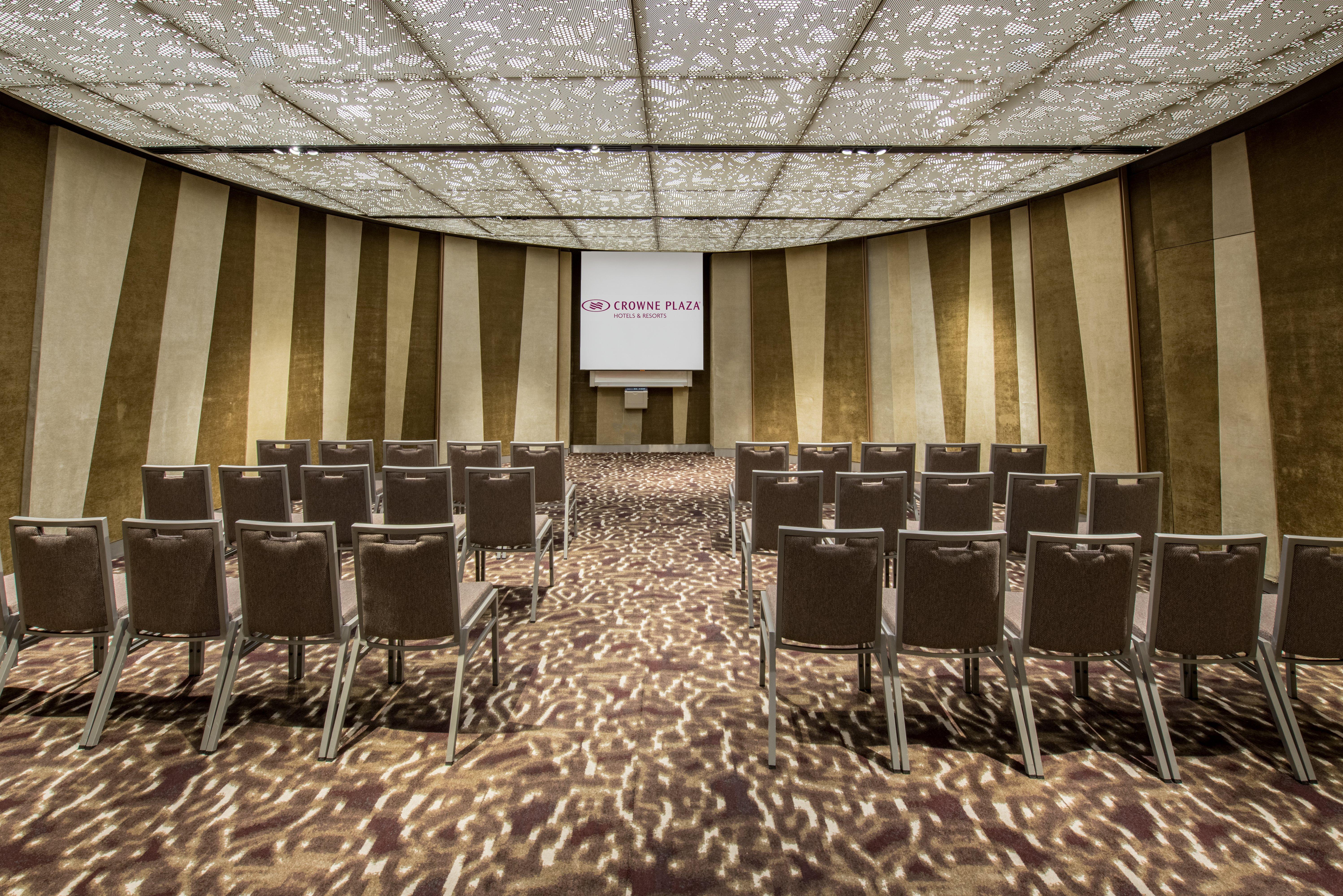 Crowne Plaza Changi Airport By Ihg Singapore Exterior photo The photo shows a conference or meeting room. It features rows of grey chairs arranged in a semi-circular layout, facing a screen at the front. The room has a decorative ceiling with a patterned design that allows light to filter through, creating in