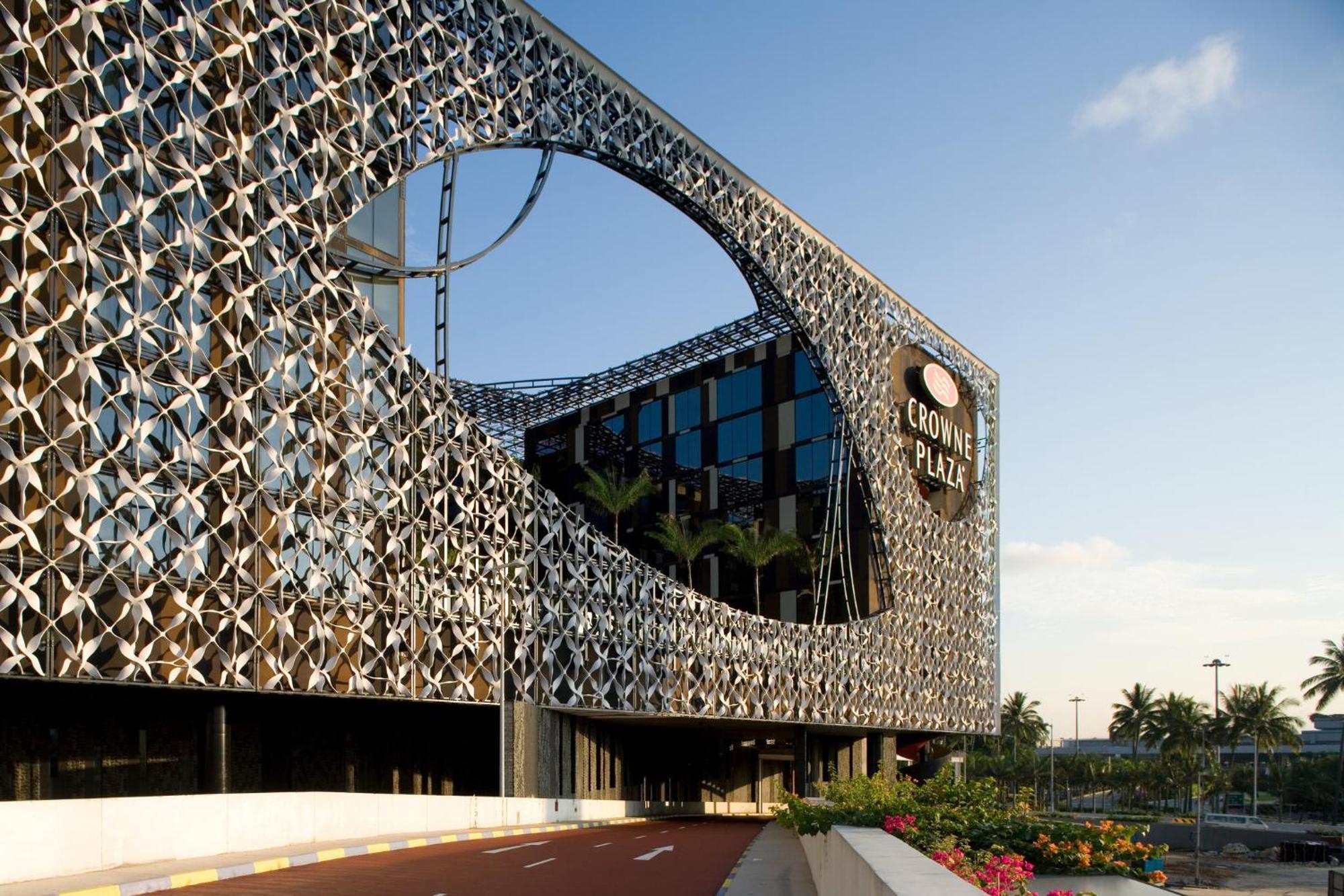 Crowne Plaza Changi Airport By Ihg Singapore Exterior photo The photo features a modern building with a unique architectural design. The facade consists of a complex lattice structure that creates a visual pattern, including a large circular cutout. The building appears to be multi-story, with large glass win