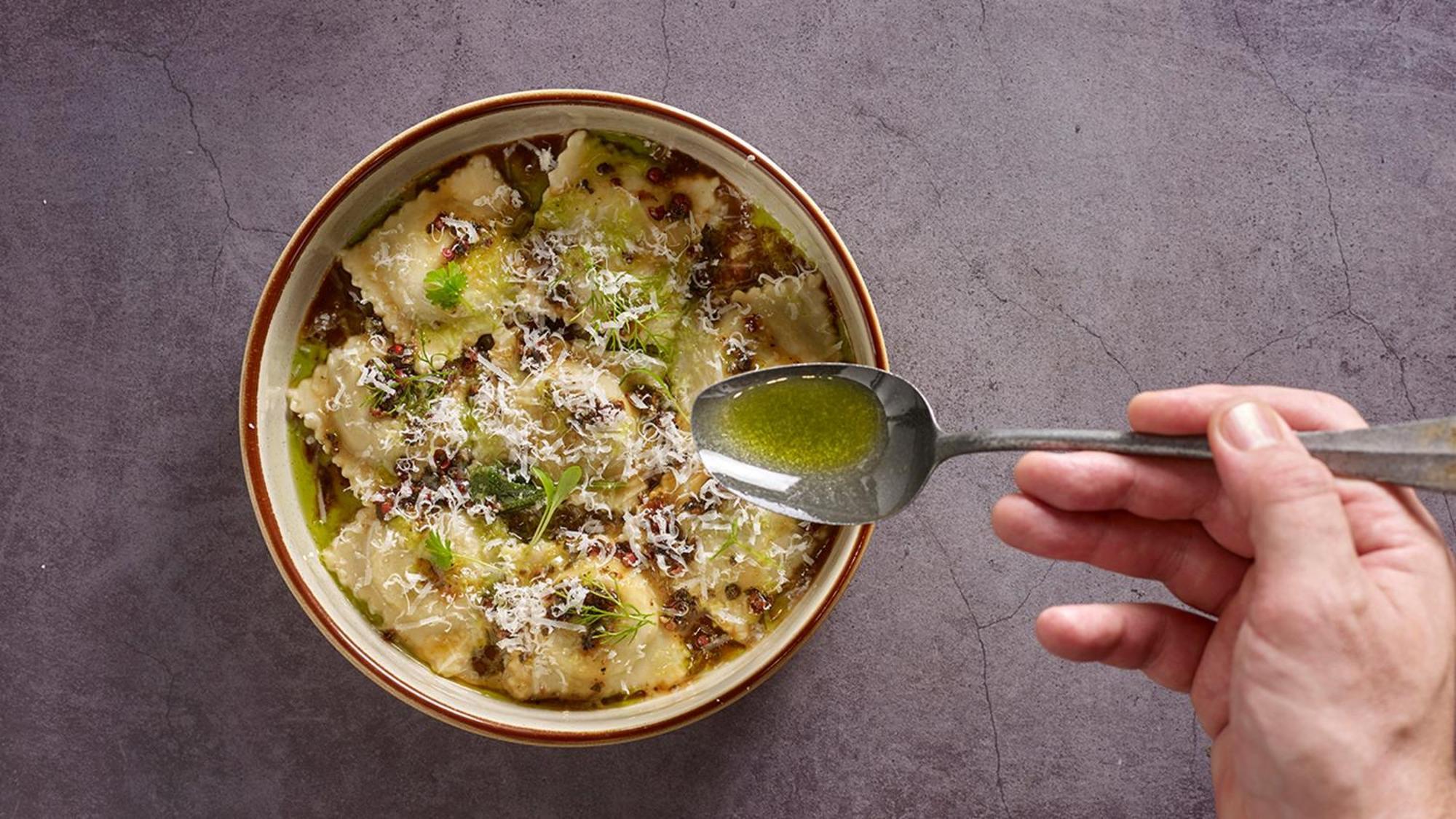 Crowne Plaza Changi Airport By Ihg Singapore Exterior photo The photo shows a bowl of ravioli garnished with grated cheese and drizzled with olive oil. A hand is holding a spoon above the bowl, indicating the action of adding more oil or sauce. The dish appears delicious and is presented with an appealing aes