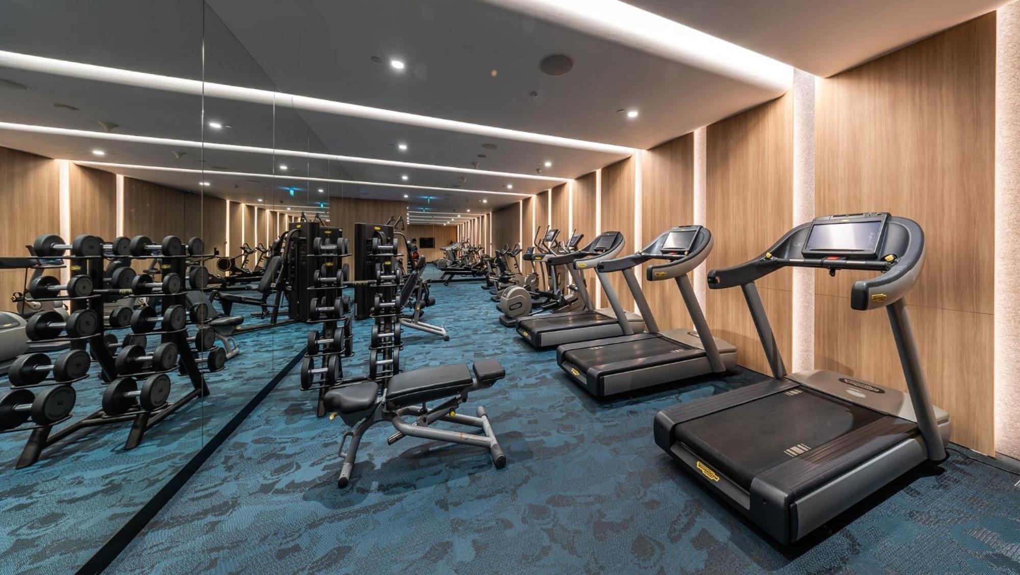 Crowne Plaza Changi Airport By Ihg Singapore Exterior photo The photo shows a well-equipped gym or fitness room. On one side, there are several weightlifting benches along with dumbbells arranged on racks. On the other side, there are multiple treadmills lined up, suggesting a space designed for both strength