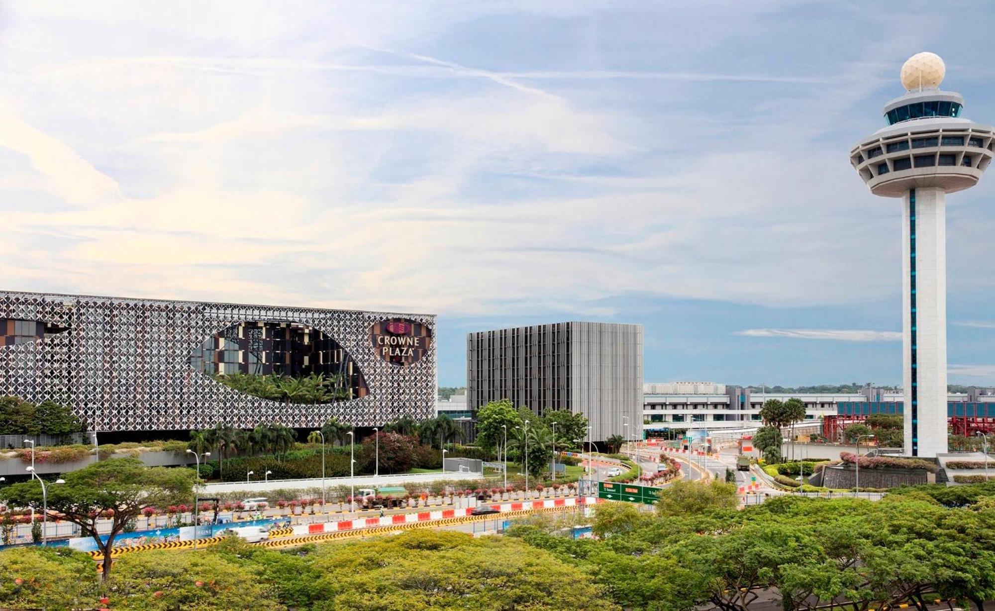 Crowne Plaza Changi Airport By Ihg Singapore Exterior photo The photo shows a modern architectural scene featuring two distinct buildings. On the left, there is a building with a unique facade that includes a large, oval opening, suggesting a contemporary design. The building appears to be surrounded by green
