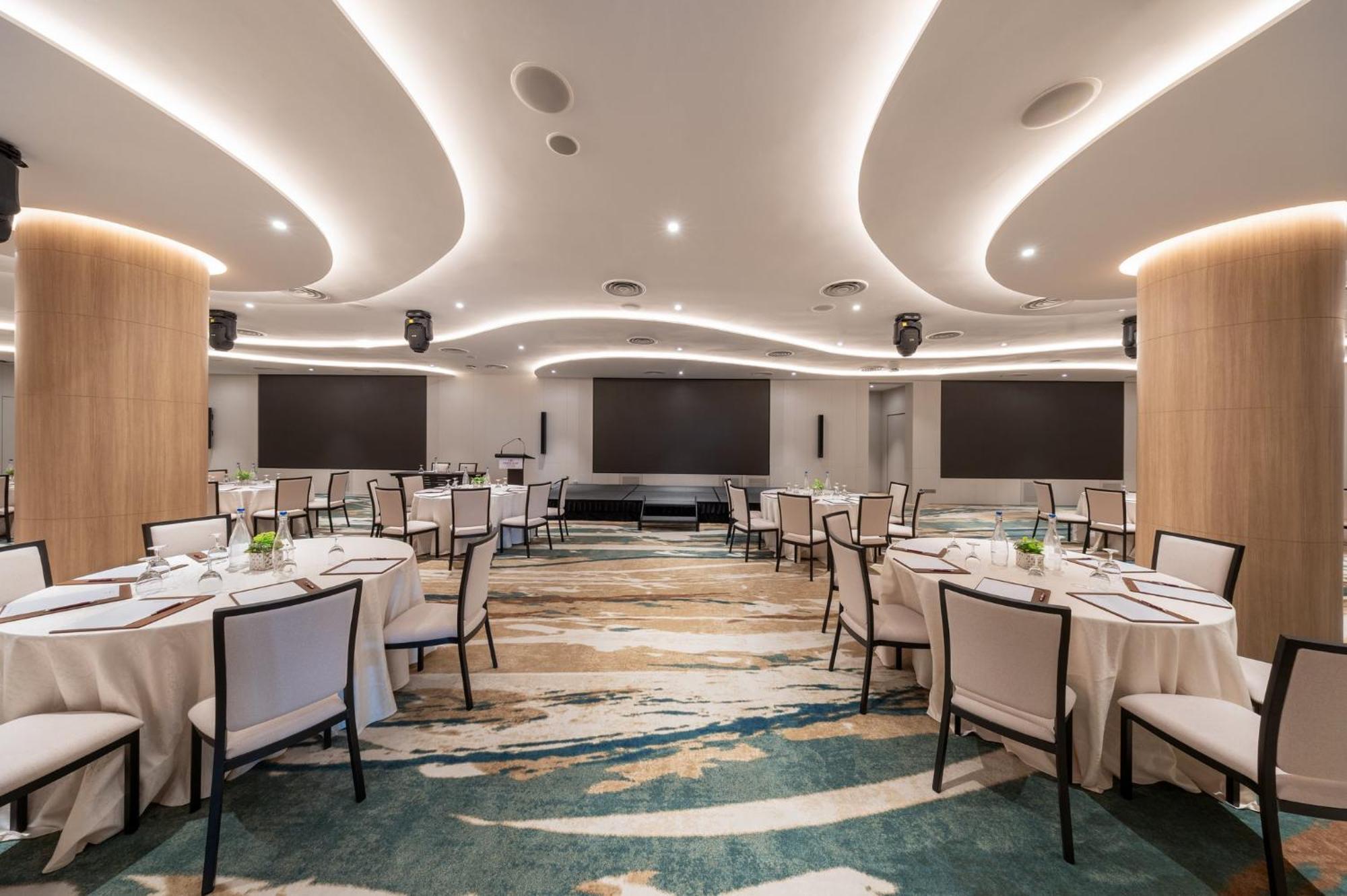 Crowne Plaza Changi Airport By Ihg Singapore Exterior photo The photo shows a modern banquet or conference room. The room features elegantly arranged round tables with white tablecloths and chairs. The flooring has an artistic design that combines various shades of blue and beige. The ceiling is accentuated w