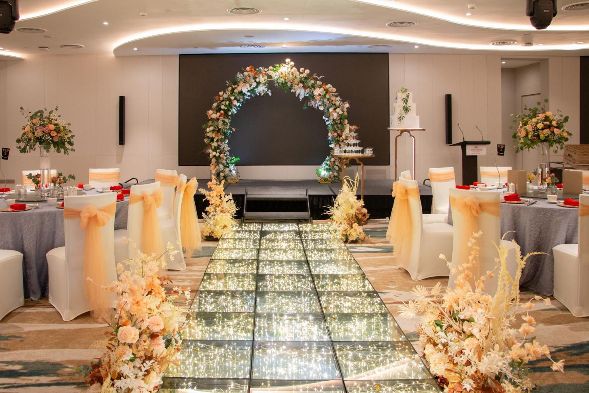 Crowne Plaza Changi Airport By Ihg Singapore Exterior photo The image depicts an elegantly decorated event space, likely for a wedding or formal occasion. In the center, there is a flower-adorned archway in warm colors, creating a focal point. A sparkling, illuminated pathway leads towards the arch, bordered 