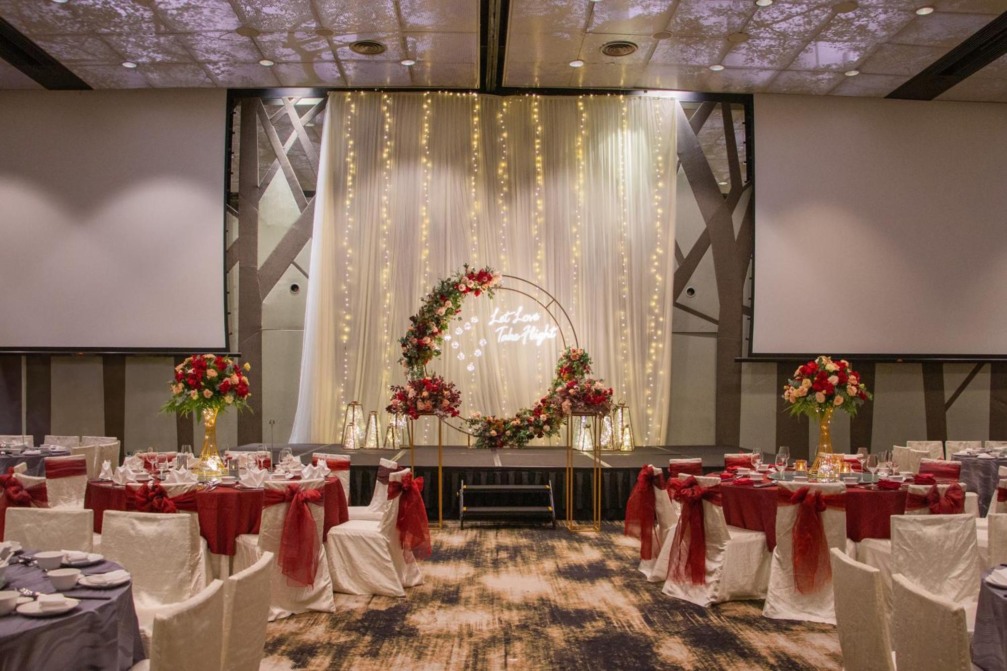 Crowne Plaza Changi Airport By Ihg Singapore Exterior photo The photo shows an elegantly decorated banquet hall set up for an event. There are round tables with white tablecloths, each adorned with a red centerpiece. The chairs have white covers and are draped with red sashes. At the back of the room, there i