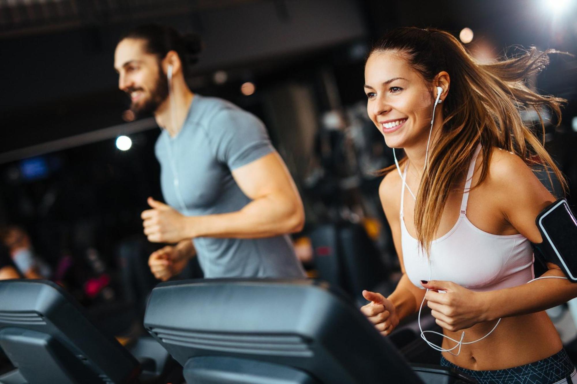 Crowne Plaza Changi Airport By Ihg Singapore Exterior photo The photo shows two individuals running on treadmills in a gym. The woman, wearing a sports bra and workout leggings, has earbuds in and is smiling as she runs. The man, next to her, wears a fitted t-shirt and appears to be focused on his workout. Bo