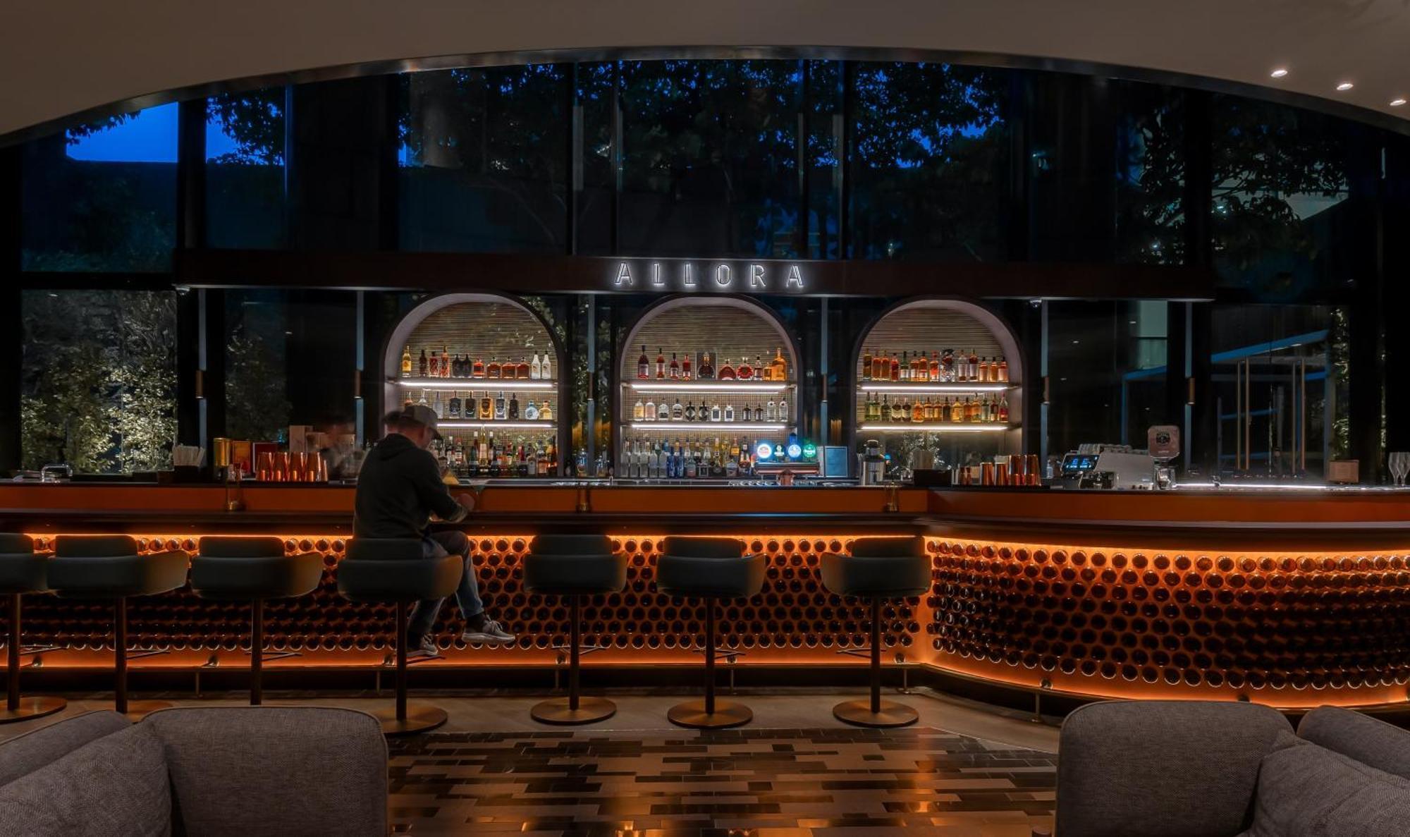Crowne Plaza Changi Airport By Ihg Singapore Exterior photo The photo shows a bar area with a modern and stylish design. In the center, there is a well-lit bar counter featuring a variety of alcoholic beverages displayed on shelves behind it. The bar has a sleek, contemporary look with circular light fixtures