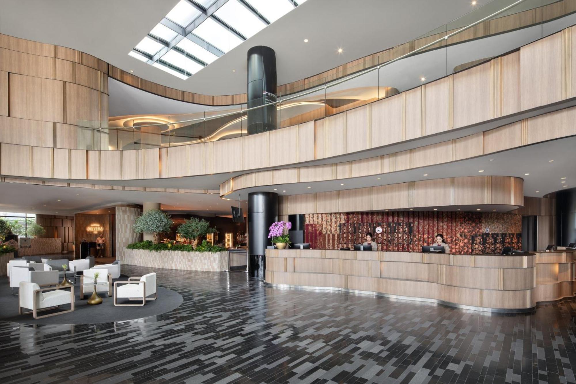 Crowne Plaza Changi Airport By Ihg Singapore Exterior photo The photo shows a modern hotel lobby with a sleek and stylish design. The reception area features a curved wooden counter, with staff members attending to guests. The interior design includes a mix of wood and stone materials, creating a warm and inv