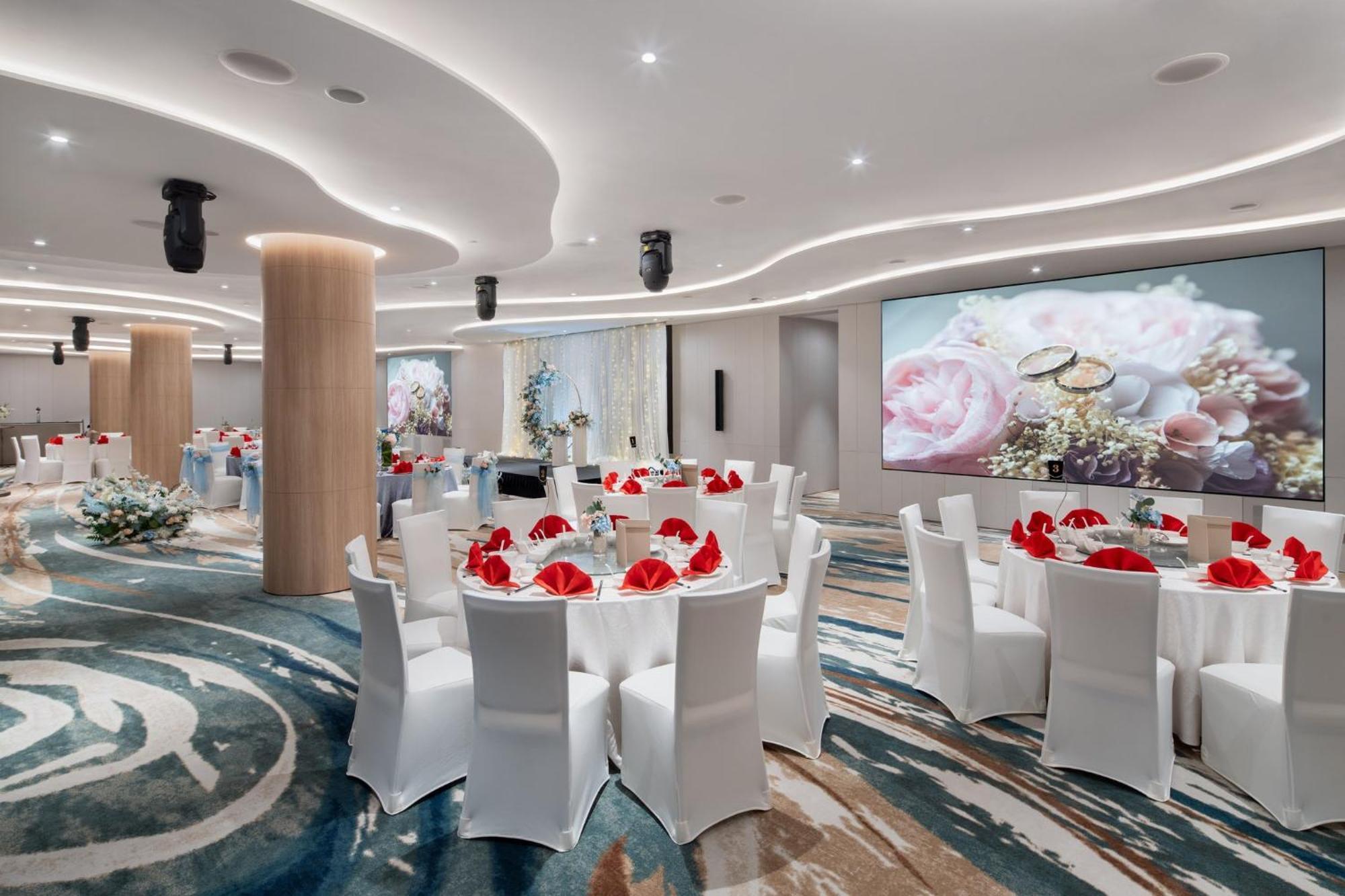 Crowne Plaza Changi Airport By Ihg Singapore Exterior photo The photo depicts an elegantly designed banquet or event hall. It features round dining tables covered with white tablecloths, each adorned with red napkins. The chairs are also white, creating a cohesive color scheme. The room has modern lighting an