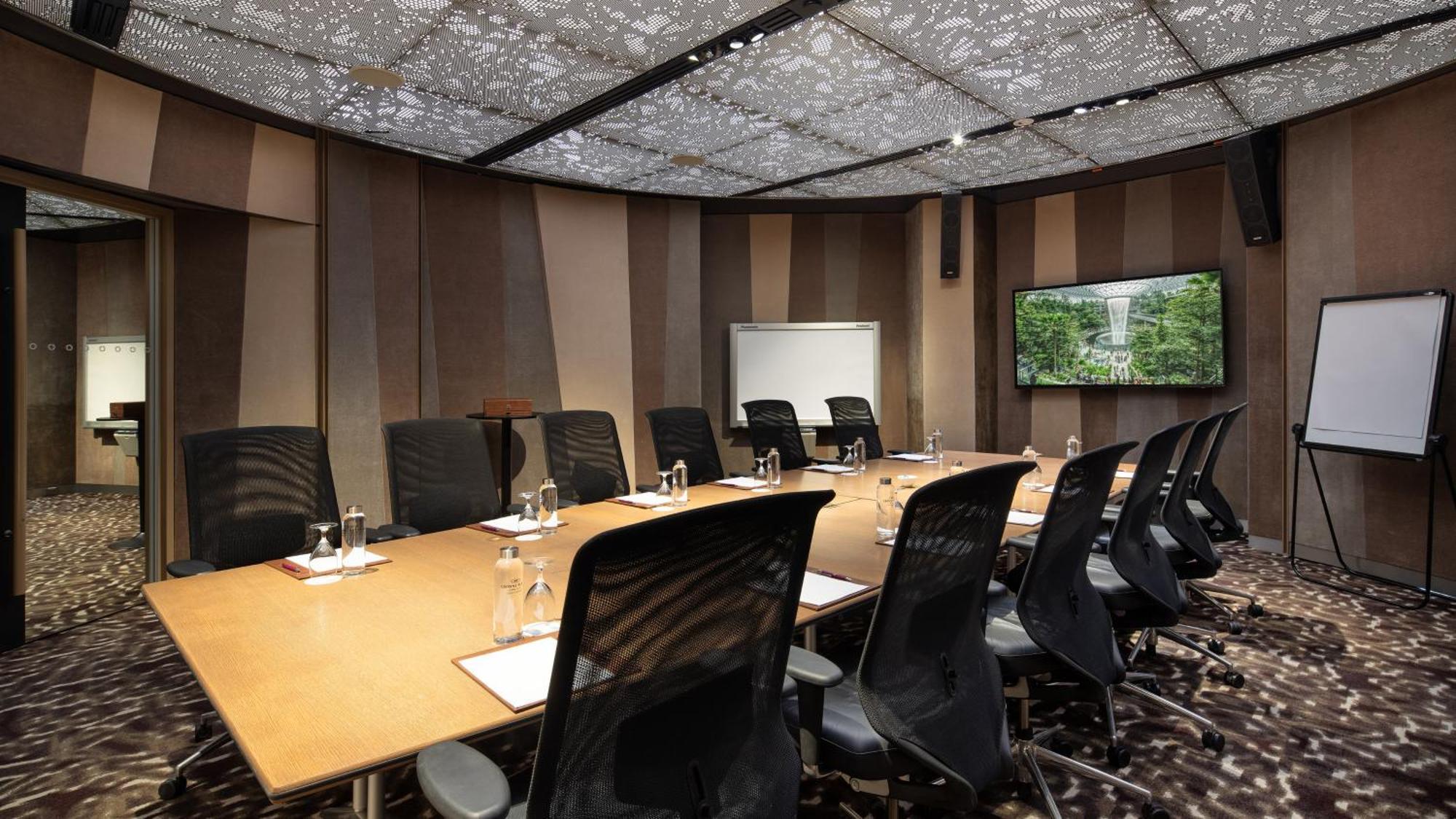 Crowne Plaza Changi Airport By Ihg Singapore Exterior photo The image shows a modern conference room. It features a large rectangular table surrounded by black ergonomic chairs. On the table, there are glasses of water, notepads, and pens. The walls have a sleek design with alternating patterns in neutral col